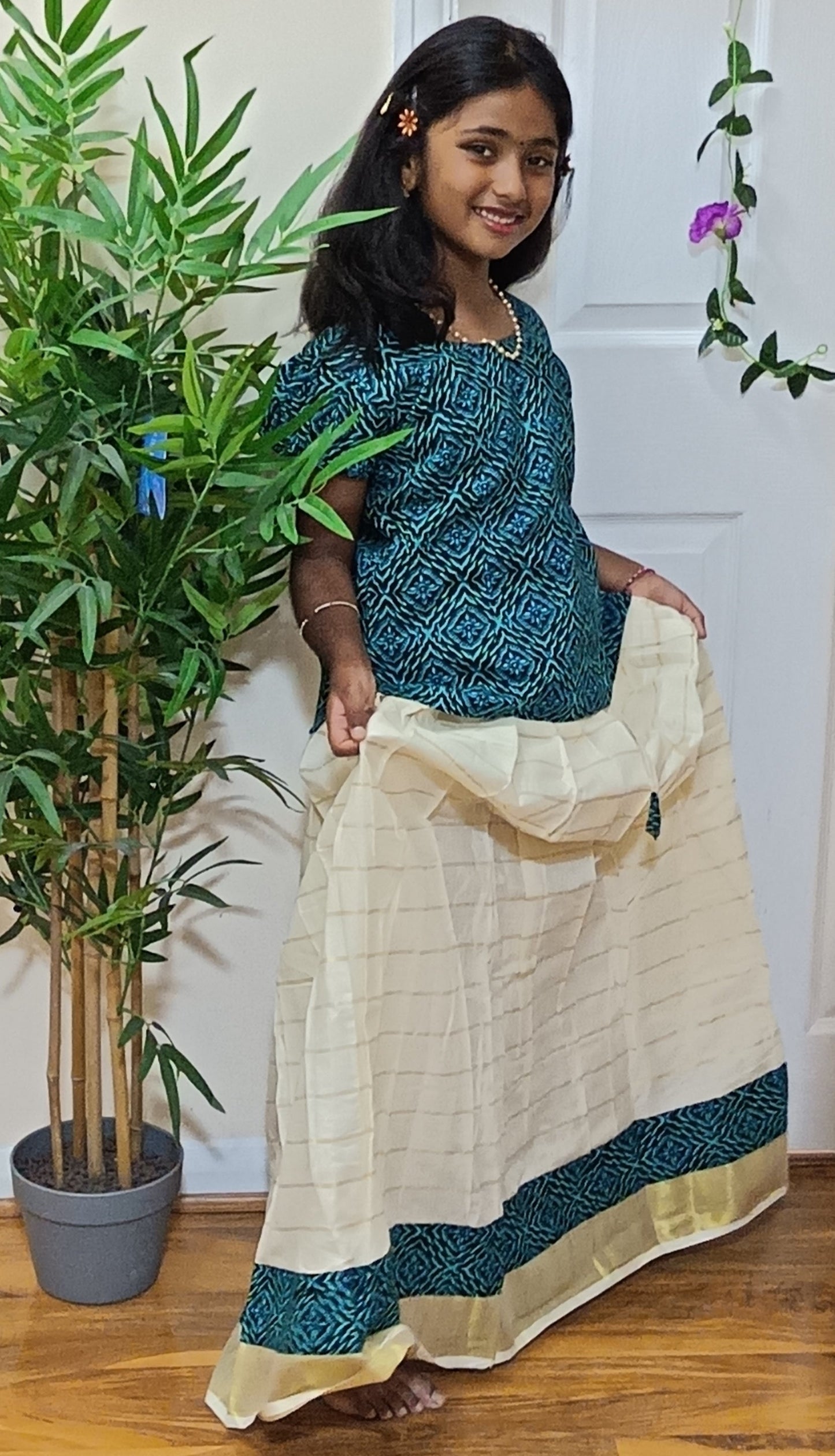 Girl posing in teal geometric block print top with cream Kerala tissue pleated skirt